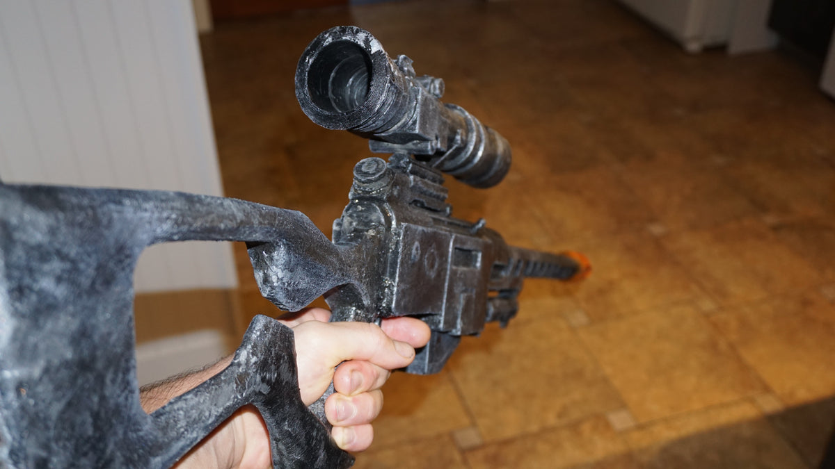 A person's hand holding a black gun with a scope attached to it.