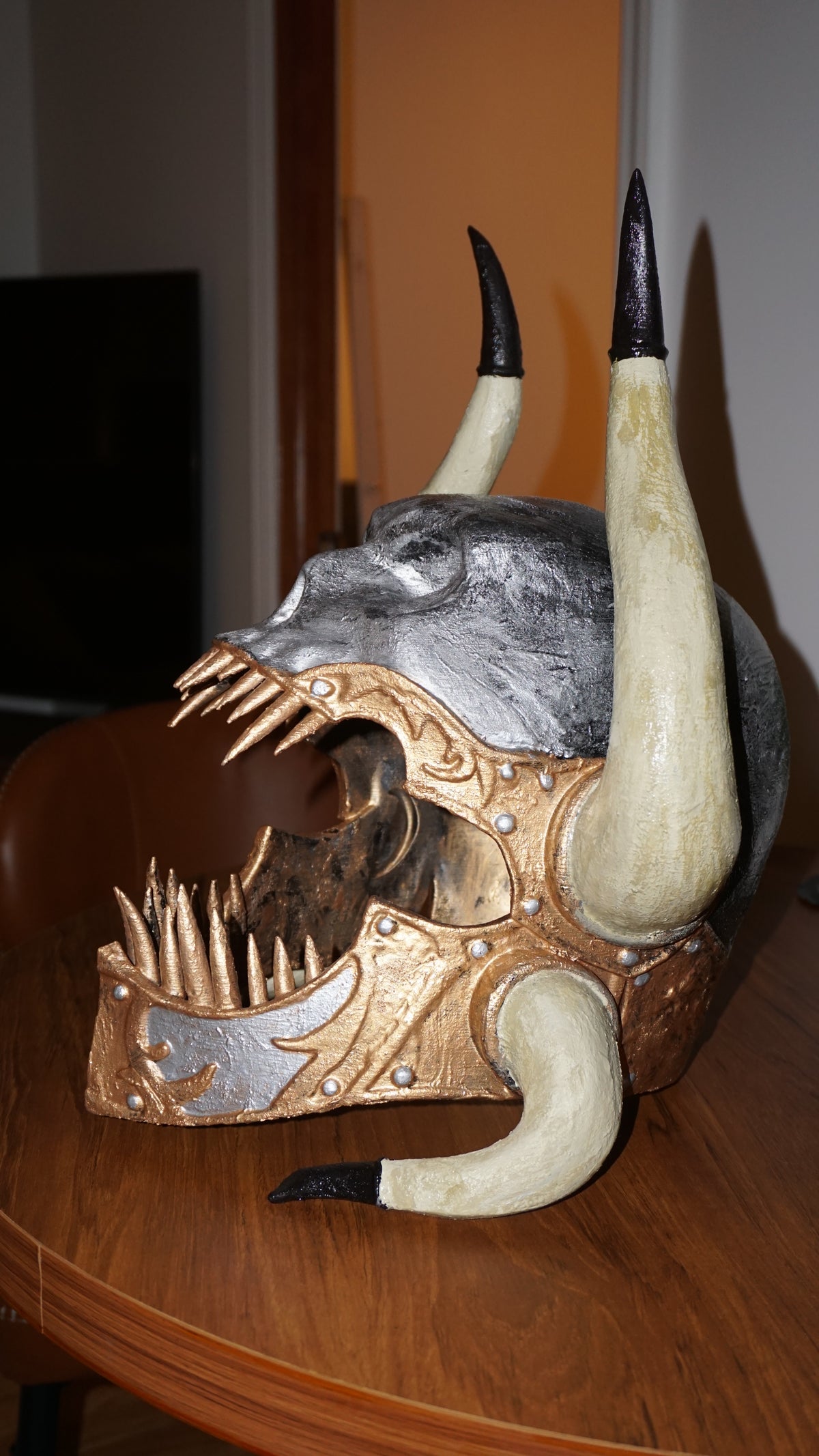 A decorative mask with sharp teeth and large horns, likely representing a mythical or fantasy creature.