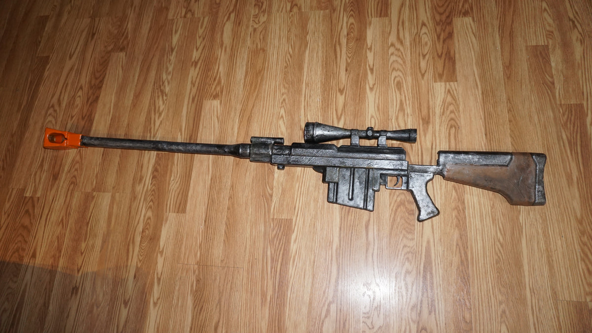 A large, black and silver toy gun with a scope and orange tip is lying on a wooden floor.